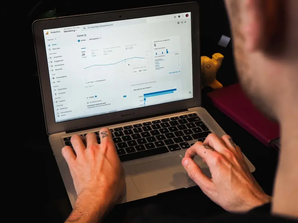 Left hand side, over the shoulder view of a man looking at a laptop, with analytics on the screen.
